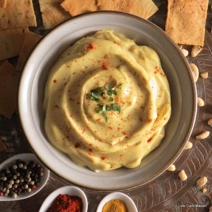Creamy curry cashew cream dip in a bowl with crackers, cashew nuts and white spoons of vibrant spices.