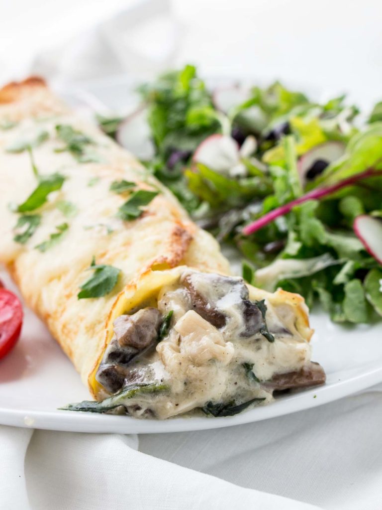 Chicken Florentine Crepes on plate with salad and tomatoes.