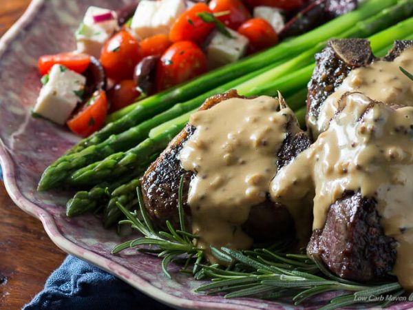 Pan seared lamb chops and rosemary with a rich mustard cream pan sauce spooned over the top on a ruffled purple plate with steamed asparagus and a Greek salad of grape tomatoes, Green olives, feta cheese, onions tossed in an herbed vinaigrette.