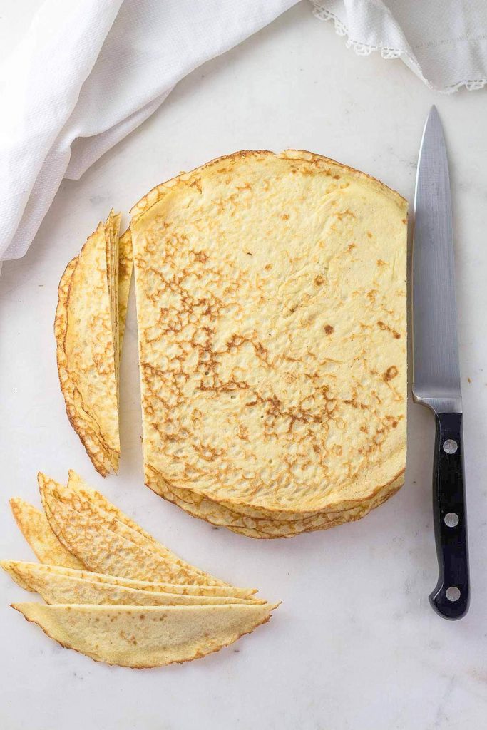 Low carb crepes for spinach manicotti with sides cut off and knife.