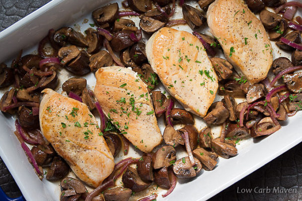 Chopped parsely spinkled over four browned chicken breasts with cooked mushrooms and purple onions in a white rectangular porcelain baking dish.