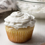 A sugar free cupcake slathered in whipped cream cheese frosting with a bowl of frosting behind.