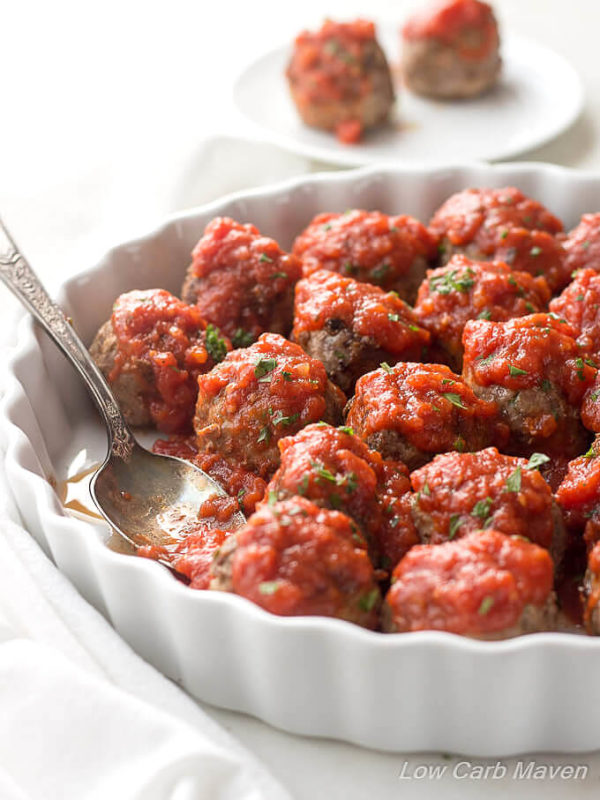 Low carb meatballs (Italian style) in Marinara sauce and sprinkled with parsley in a white scalloped dish with a sauced spoon in a place where a meatball once sat.
