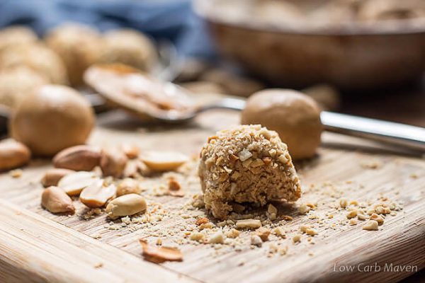 low carb peanut butter balls rolled in chopped peanuts on a cutting board.
