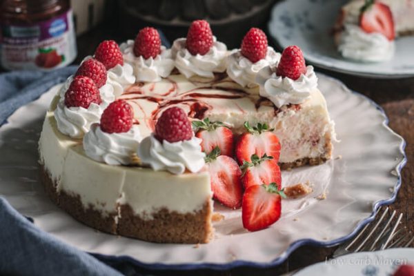 Strawberry and raspberry swirl cheesecake with whipped cream, fresh raspberries and strawberries on a plate.