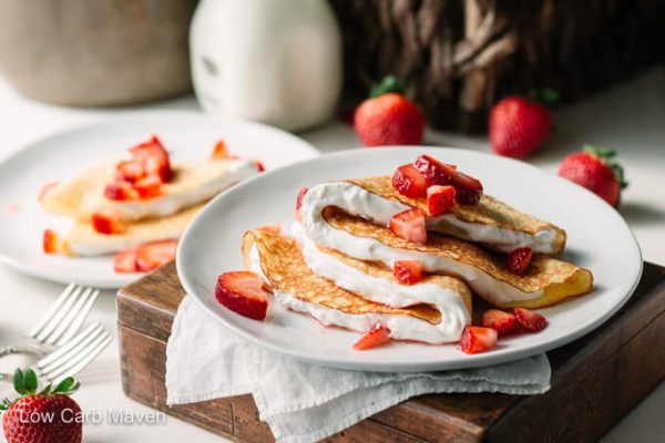 Folded Keto strawberry crepes and whipped cream on a plate with napkin.