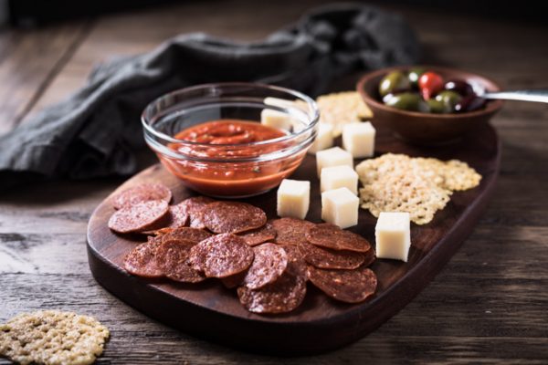 Pepperoni chips, cheese cubes, and Marinara sauce on a cutting board.