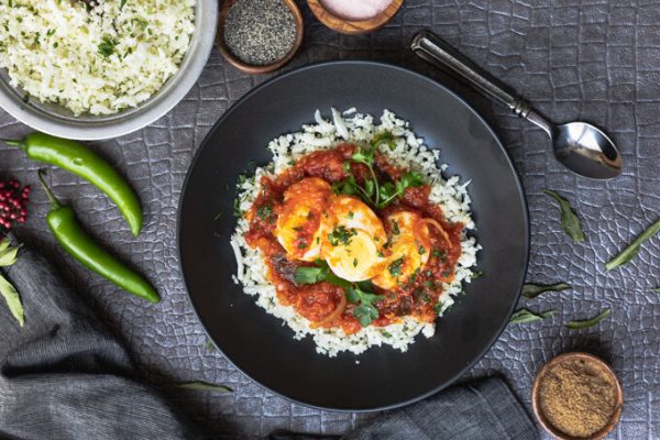 Keto egg masala or egg curry with cauliflower rice in a bowl with spoon.