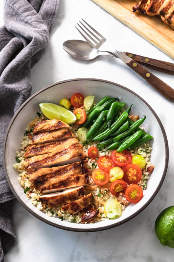 Sliced Key West chicken breast on cauliflower pilaf with vegetables in a bowl.