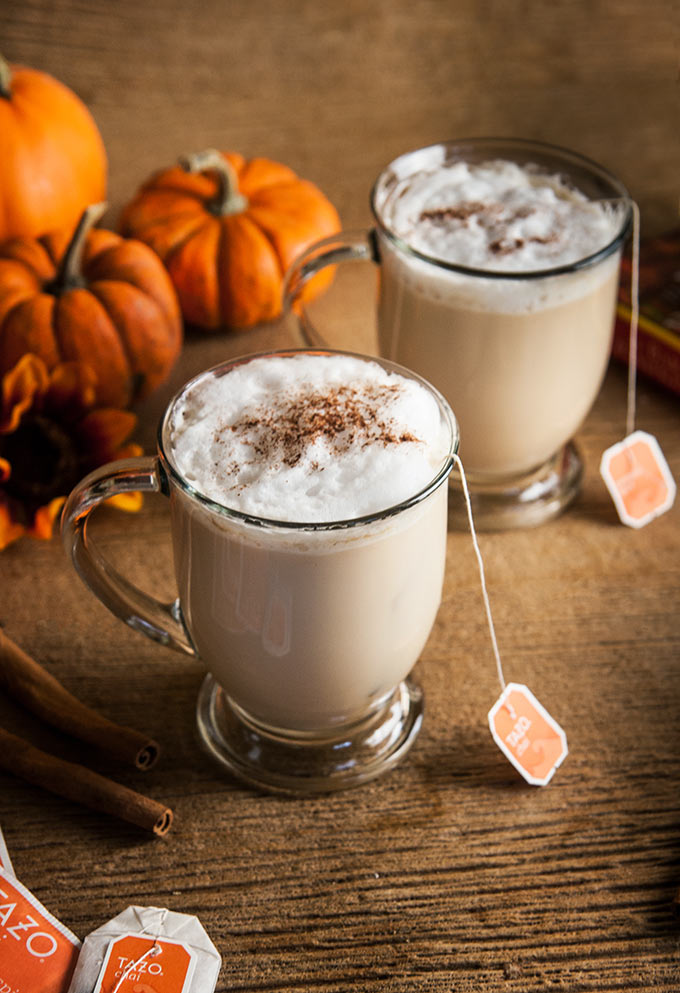 2 Pumpkin Spice Chai Lattes with cinnamon stick s, pumpkins, and florals and pumpkin spice syrup on wood