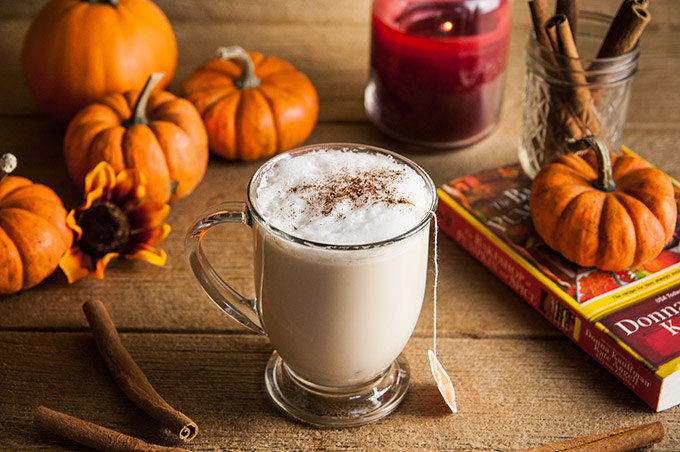 A pumpkin spice chai latte with cinnamon stick s, pumpkins, and florals and pumpkin spice syrup on wood