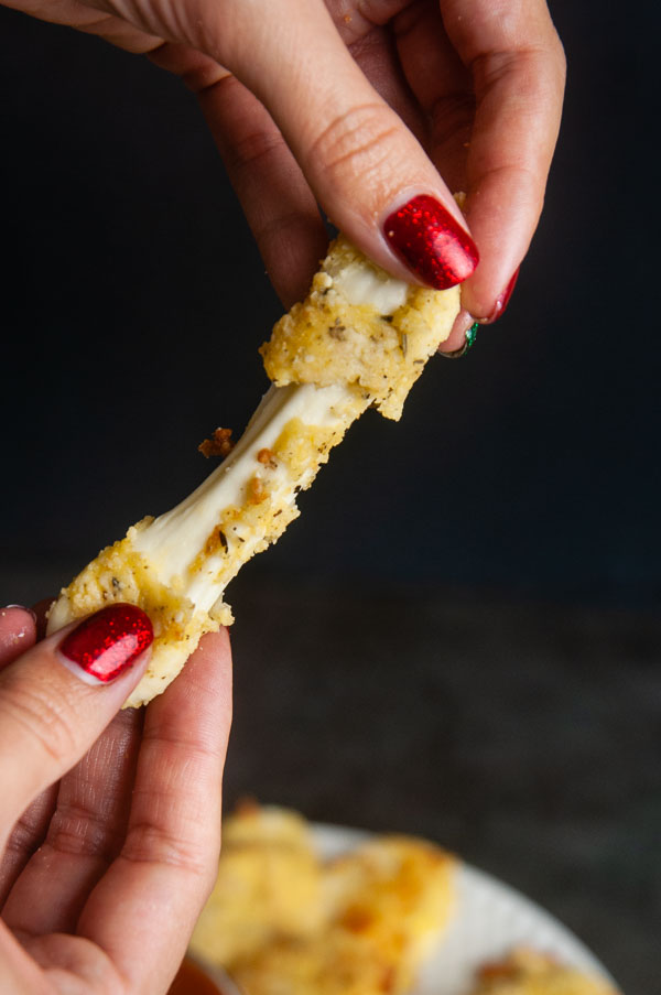 Low carb mozzarella stick being stretched apart by two female hands on black