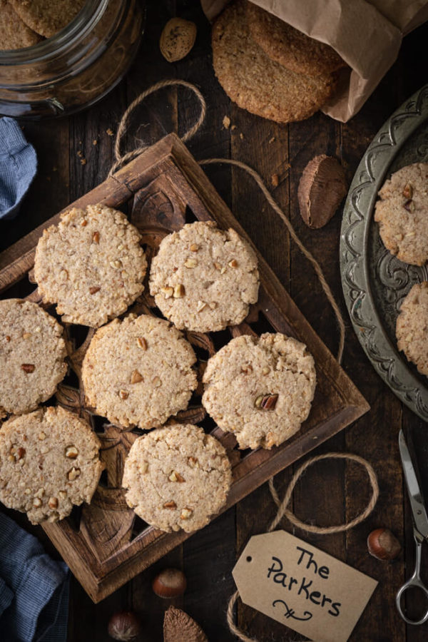 Pecan sandies cookies on a trivet with more on a platter with nuts and twine around