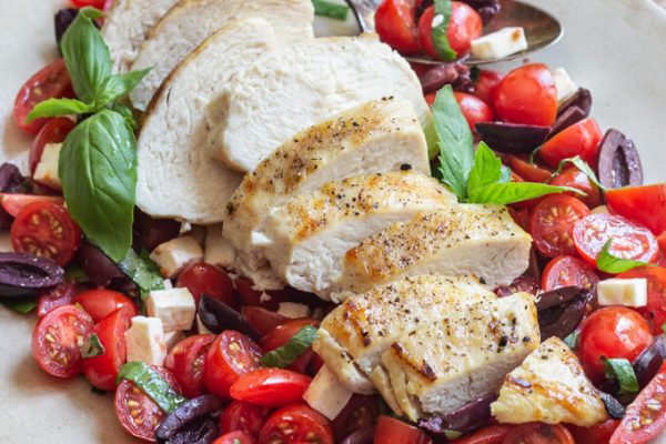 Sliced grilled chicken on a tomato salad including basil, mint, kalamata olives and feta cheese.