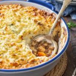 Baked keto shepherd's pie with mashed cauliflower topping in blue rimmed casserole dish with spoon.