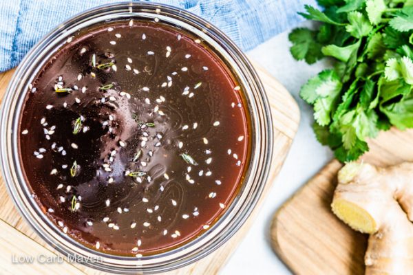 Sugar free teriyaki sauce with sesame seeds in bowl with blue napkin at top with ginger and cilantro at right.